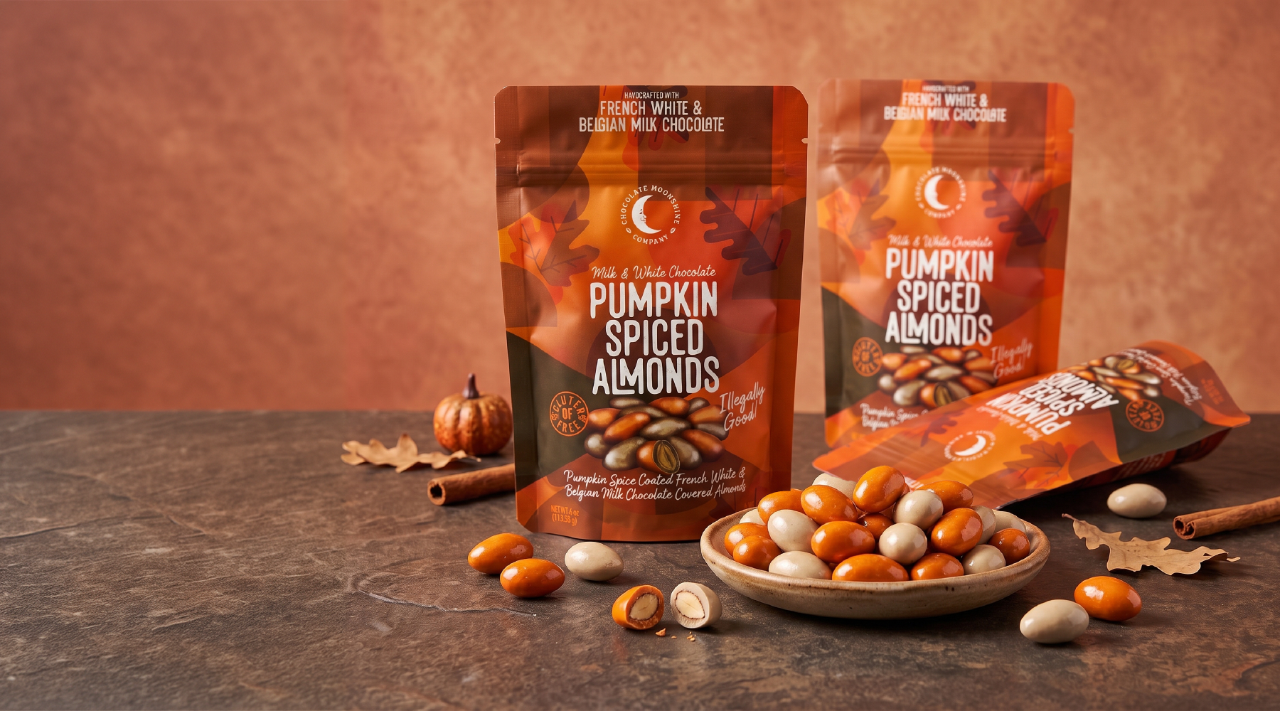 Bags and a bowl of Chocolate Moonshine Pumpkin Spiced Almonds with fall seasonal decor